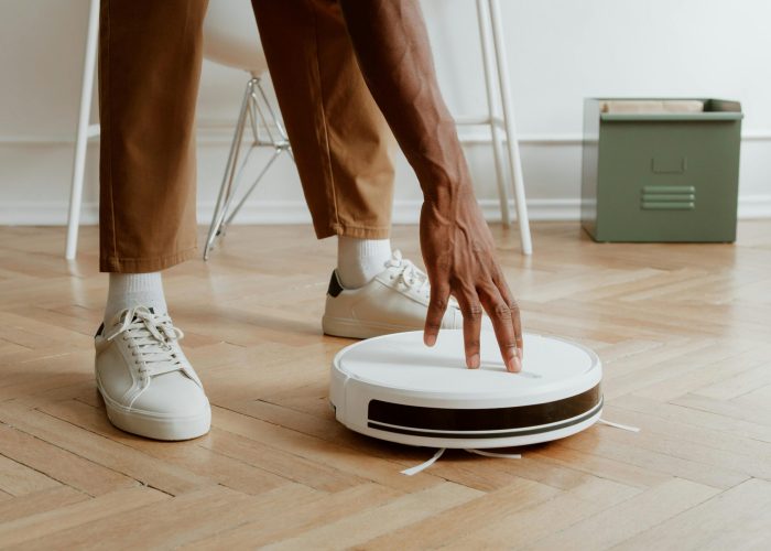 A man's hand adjusting a robot vacuum on a wooden floor in a modern home interior.