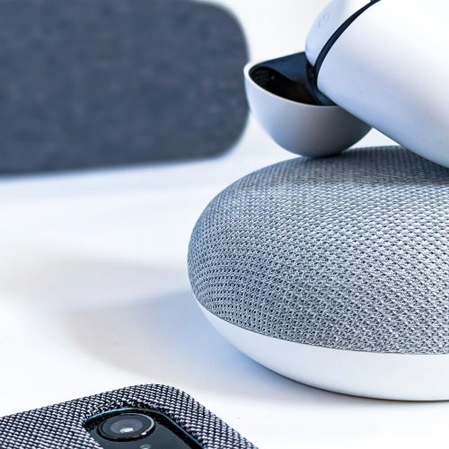 Close-up of wireless earbuds, smartphone, and smart speaker illustrating contemporary tech design.