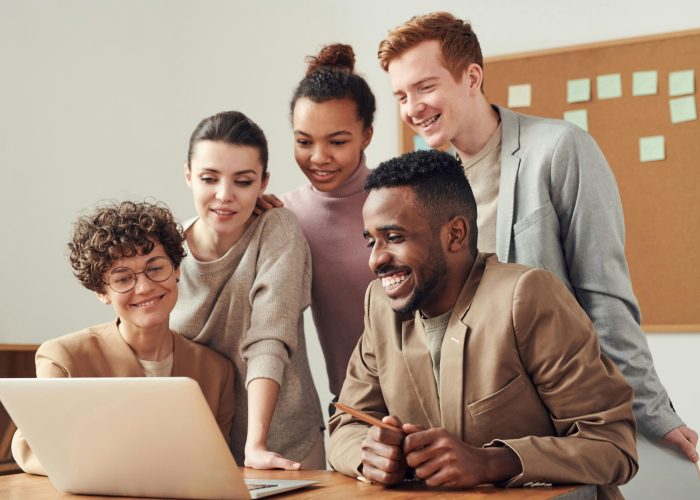 A group of diverse young professionals happily collaborating around a laptop indoors.